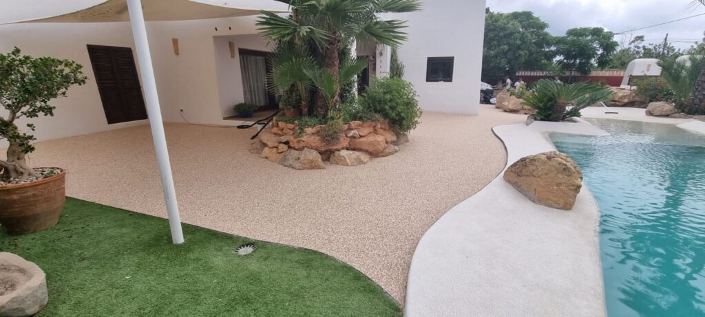 Zona completa de piscina con jardín y pavimento de árido en dos tonalidades